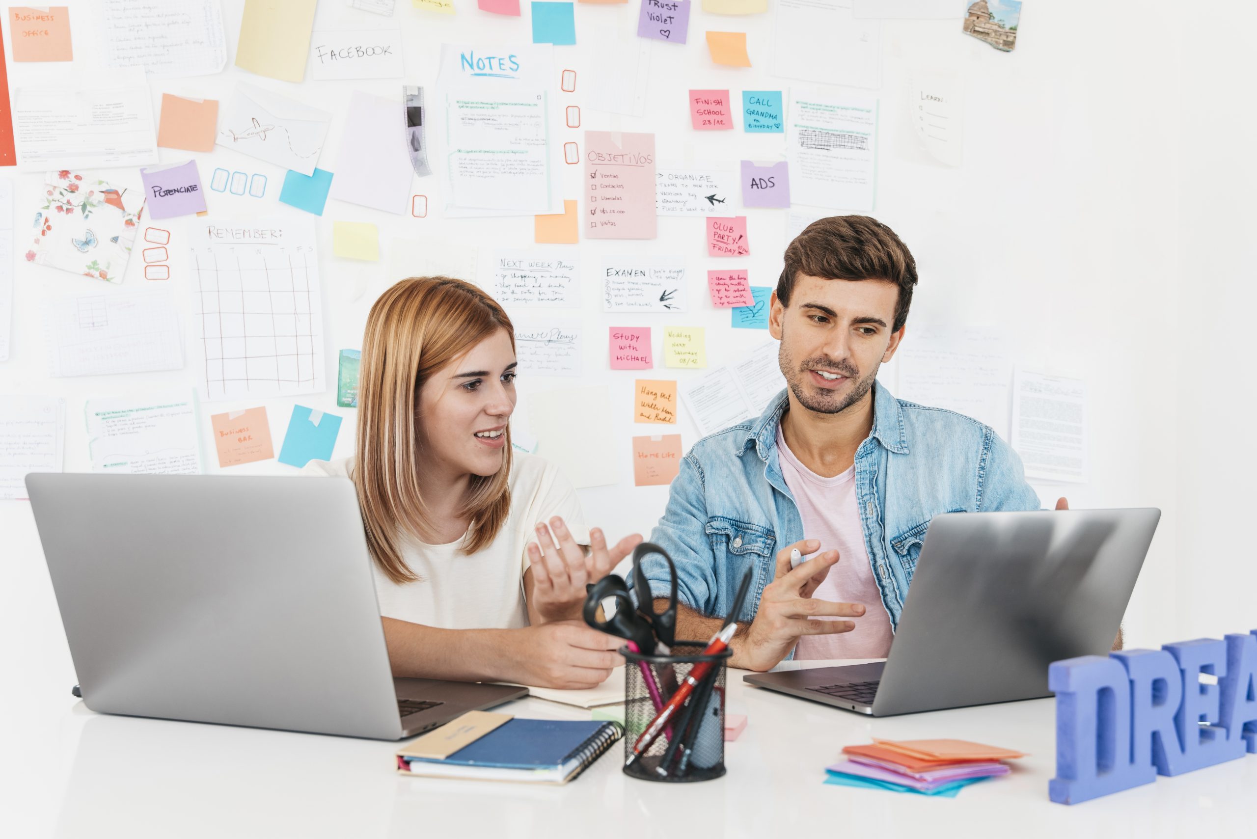 smiling-male-female-sitting-desk-talking-looking-laptop